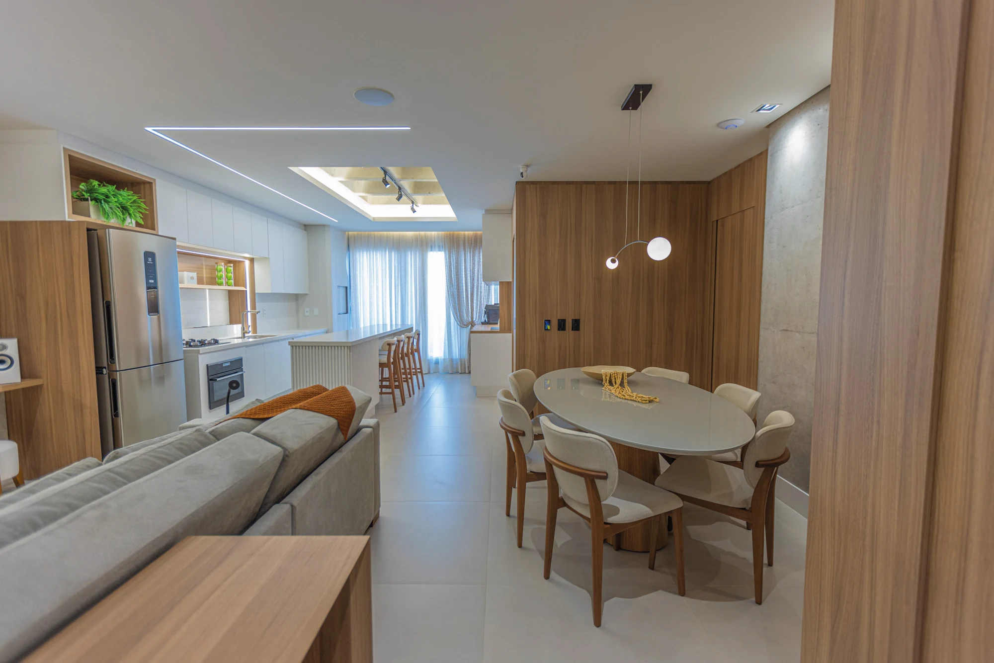 Ambientes integrados do decorado 902, com sofá cinza, mesa de jantar e painéis de madeira