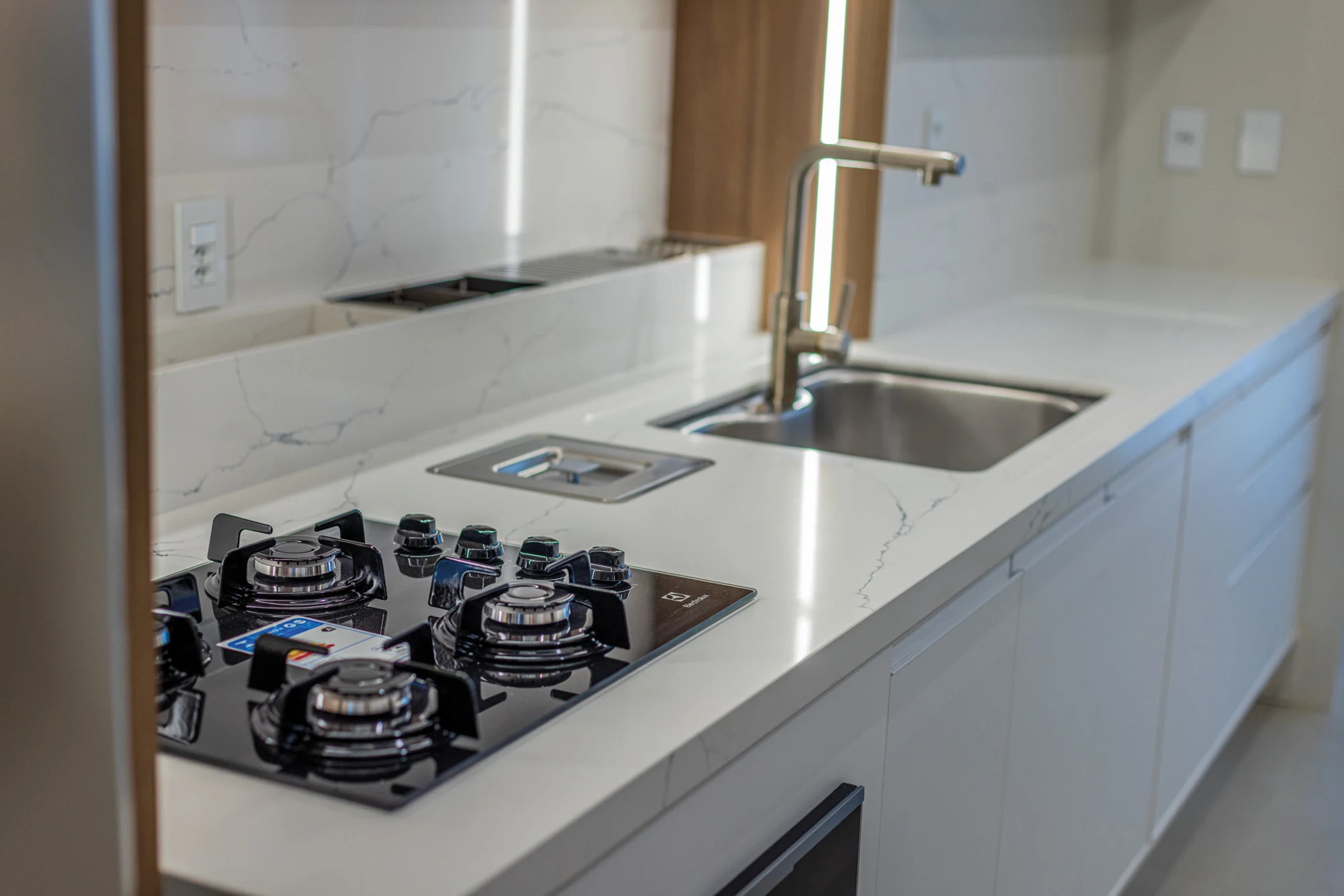 Bancada da cozinha com cooktop, cuba e superfícies claras