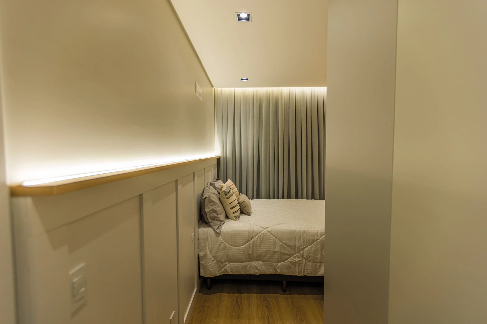 Dormitório em tons claros com iluminação indireta e cortinas