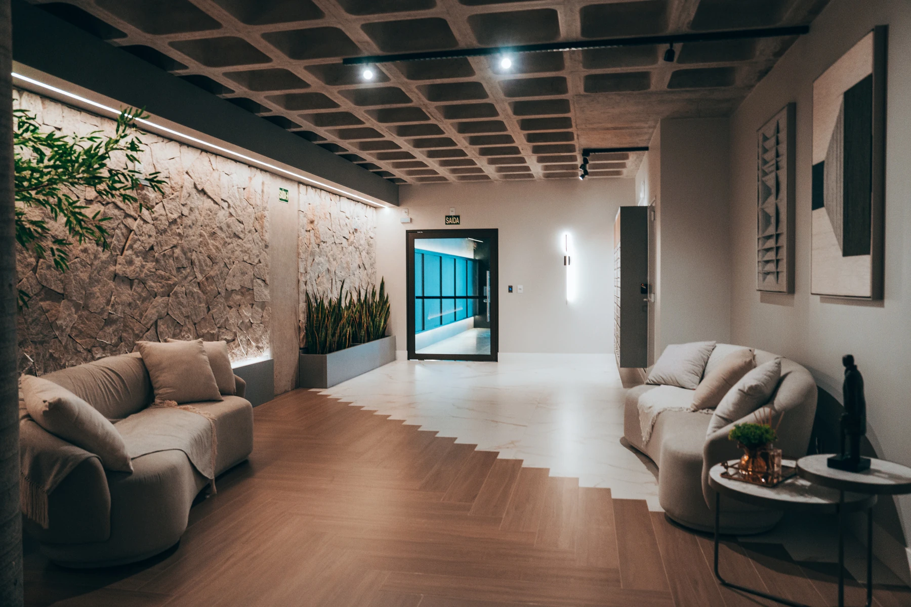 Hall do Residencial Champagnat, com teto de madeira, parede de pedra e poltronas claras
