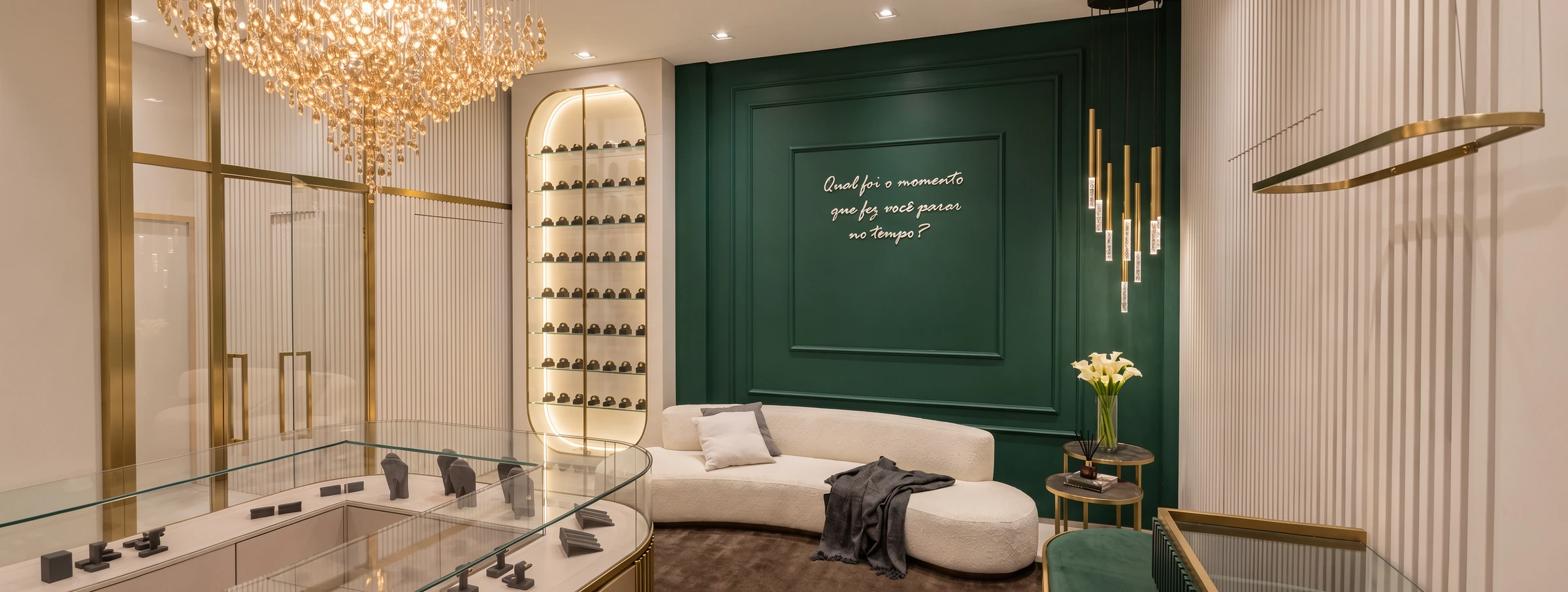 Sofá curvo claro diante de painel verde profundo, ao lado de vitrine com iluminação em arco e lustre de cristais